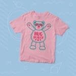 A kids' pink t-shirt with a teddy bear on it and the phrase "HUG DEALER" printed on it:
Product Name: Kids "HUG DEALER" Fine Jersey Tee
