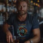 A man with a beard sitting at a bar with a drink.