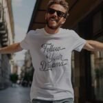 Man in a white Follow Your Dreams | Unisex T-shirt walking on a city street.