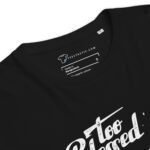 Close-up of the neckline of a black "To Blessed To Be Stress | Unisex Organic Cotton T-shirt" with a label showing the brand "Teestastic," indicating it is made in Bangladesh and is size S. Part of a graphic text design, stating "Blessed To Be Stress," is visible on the front of the shirt.
