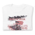 White unisex t-shirt from the "American Dream | Guns, Bikes & MAGA" collection, showcasing motorcyclists riding on a desert road. One rider holds an American flag, and above the image is the text "AMERICAN DREAM," evoking a sense of freedom and adventure.