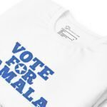 VOTE FOR KAMALA unisex t-shirt for Elections 2024, featuring blue text "Vote For Kamala," neatly folded on a surface. The shirt label displays the brand name and size details, making it an ideal choice for showing your support in the upcoming elections.
