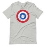 The "Star and Stripes | Red Captain America | Unisex T-shirt" showcases a distressed graphic of Captain America's shield with a blue circle and white star at the center, encircled by white and red concentric rings on a gray fabric.
