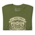 A folded All Good Things Are Wild And Free Unisex Heavy Cotton Tee in olive green showcases a nature-inspired design, with the words "All Good Things Are Wild And Free" and "Respect Nature" elegantly printed in beige.