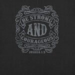 The BE STRONG AND COURAGEOUS | Unisex T-shirt features ornate text on a dark background boldly proclaiming "BE STRONG AND COURAGEOUS, Joshua 1:9" with striking detail. This piece is both an inspirational and timeless statement of faith suitable for any wardrobe.