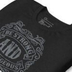 The BE STRONG AND COURAGEOUS unisex T-shirt, available in black, features a stylish decorative design with the phrase "Be Strong and Courageous" elegantly printed in light gray. The label is subtly placed at the neck for a blend of style and comfort suitable for everyone.